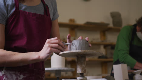 mid section of female potter wearing apron using ribbon tool to create design on pot at pottery stud