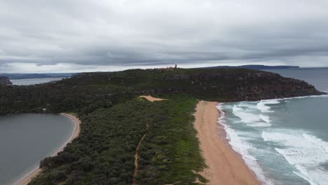 Drone-Ascendiendo-Sobre-Una-Península-Que-Revela-Una-Playa-De-Arena-A-Un-Lado-Y-Una-Bahía-Al-Otro