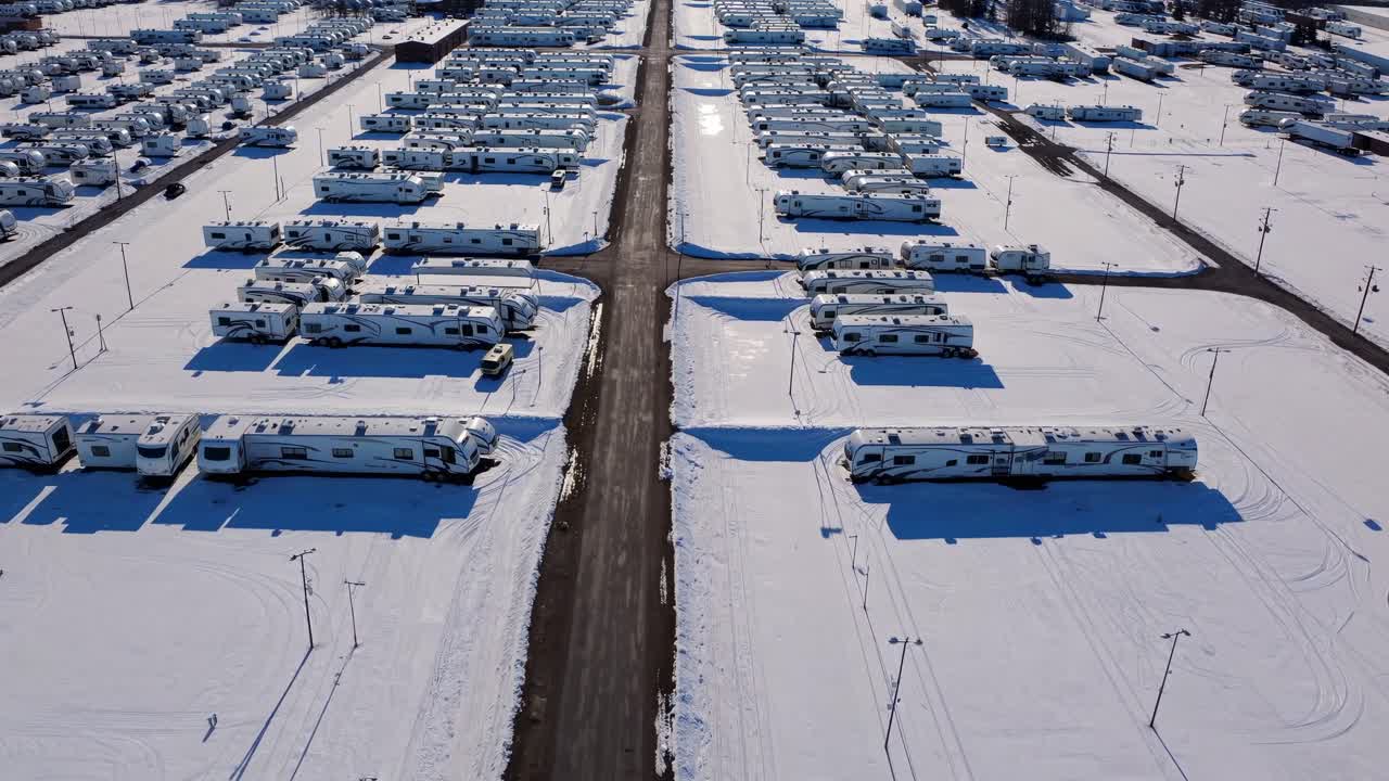 Aerial perspective captures snow-blanketed RV park with parked vehicles along a winding road, emphasizing winter scenery and tranquil environment