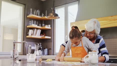 Grandmother-and-little-girl-in-apron-flattening-dough-with-rolling-pin-4K-4k