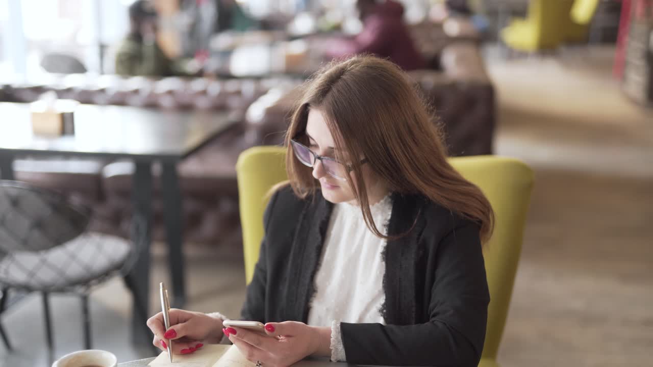 Woman taking notes in a coffee shop before receiving phone call