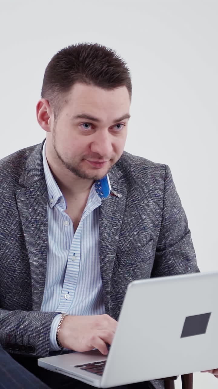 Businessman working on a laptop. Man in stylish costume looking into the laptop and becomes happy on white background. Slow motion. Vertical video