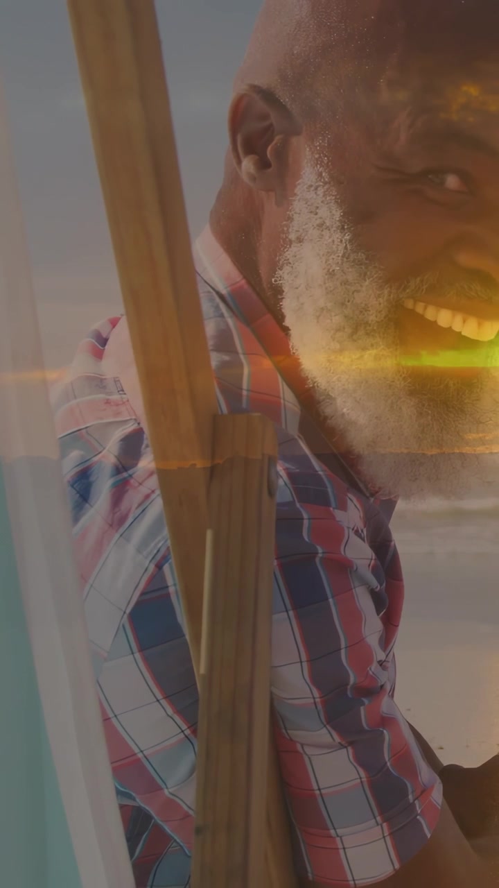 Vertical video: Camera pan, man turning, sunlight streaking over easel, smile forming for portrait