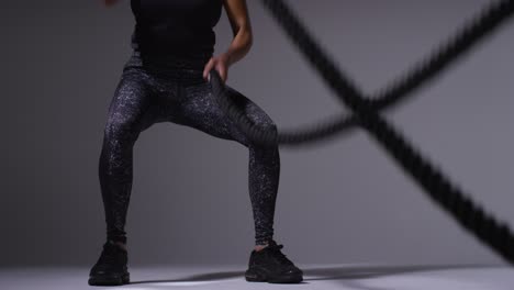 close up studio shot of mature woman wearing gym fitness clothing doing cardio exercise with battle ropes 2