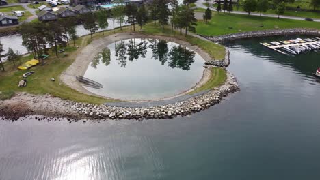 Unique-artificial-circular-pond-for-swimming-in-Kinsarvik-Norway---Aerial-with-tilt-down-and-mirror-like-reflections-in-sea-surface