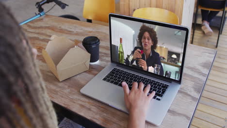 mujer tomando un bocadillo mientras hace una videollamada en una computadora portátil en una cafetería