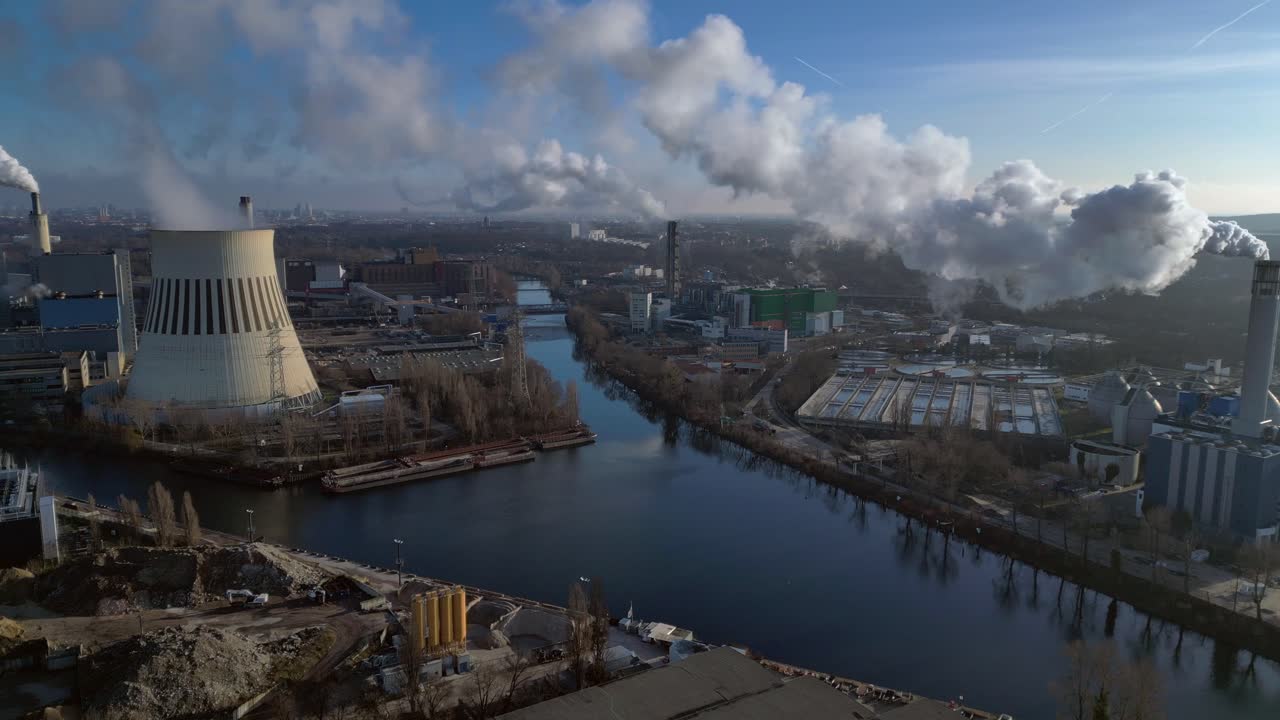 large industrial power plant emitting large amounts of smoke over the city Berlin next to a river on a sunny day. Unique aerial view flight