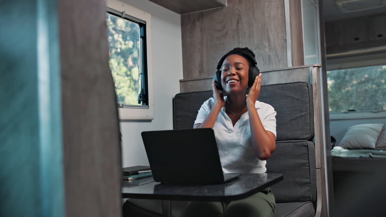 Young Black Woman Laughing While Using Laptop and Headphones in RV