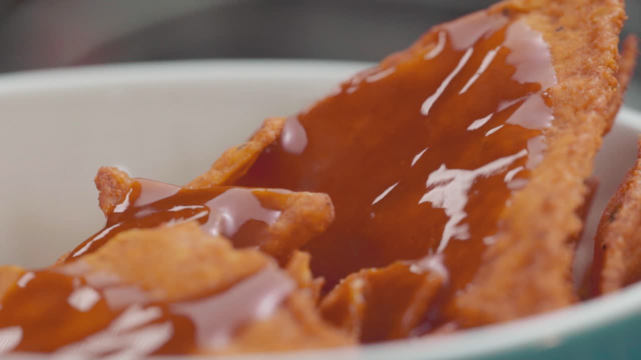 Adding spicy red sauce to nachos while the plate rotates. Close-up