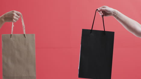 video of hands of caucasian women holding shopping bags with copy space on red background