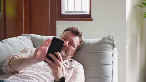 relaxing at home, senior man using smartphone on comfortable sofa