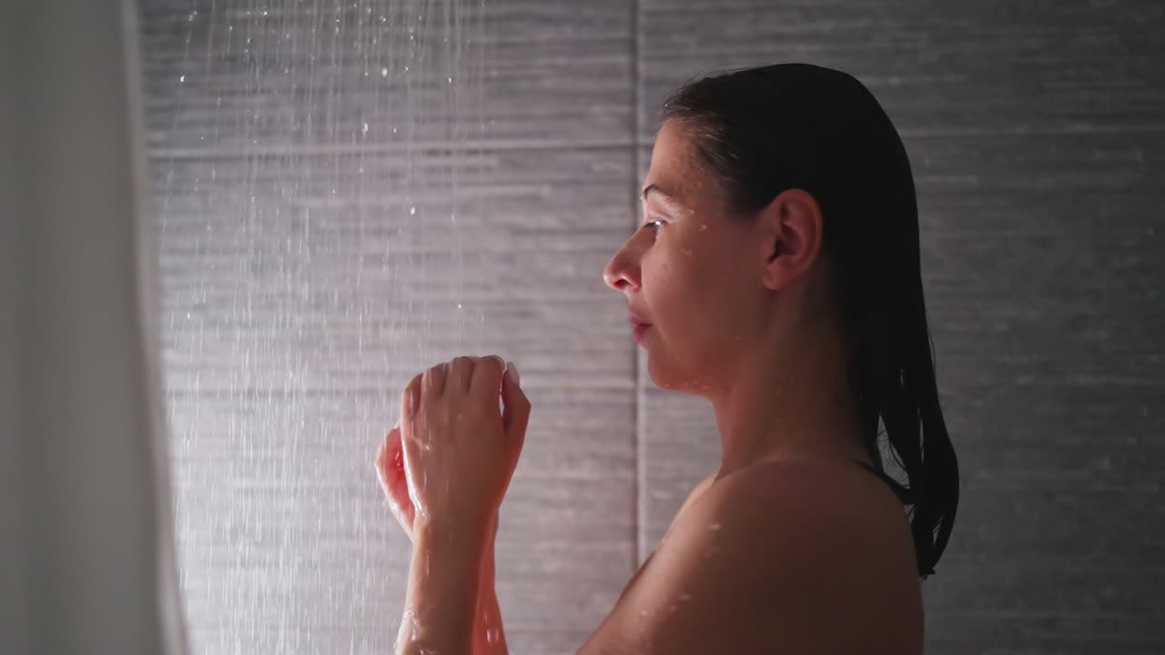 mujer calienta las manos en el agua de la ducha en el baño. dama morena con los hombros desnudos lava las palmas con gotas de líquido caliente en el lavabo. relajación en el spa