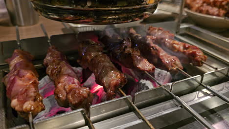 auto turning skewers, lamb bbq cooking automation - lamb meat on skewers roasted on live coals automatically spun with an electric machine for even roast in korean restaurant - close-up