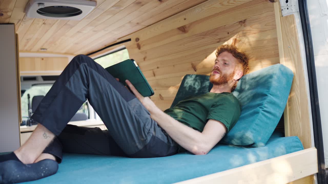 Man Relaxing in a Campervan Reading a Tablet