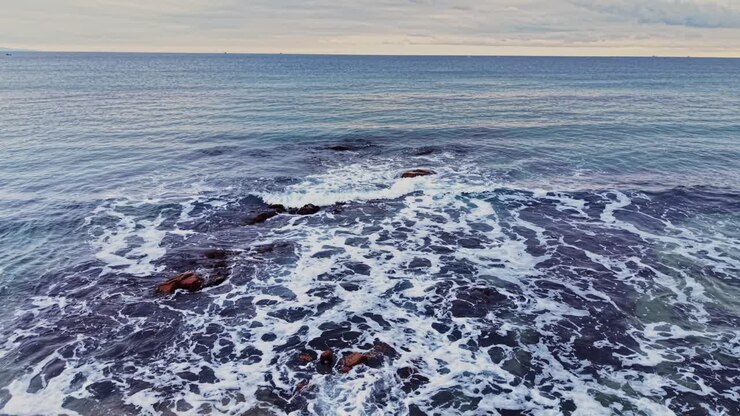View of calm ocean waves breaking on rocky shore at sunset