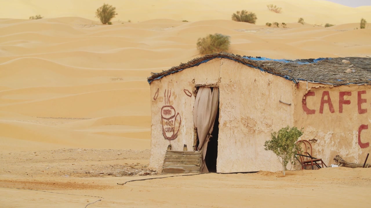 Piccolo edificio tradizionale di un caffè nel deserto isolato tra le dune di sabbia del Sahara vicino a Ksar Ghilane, Tunisia, che riflette l'architettura e l'ospitalità locale