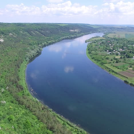 a wide blue river flows between rocks with trees and countryside with long fields and a private sector. aerial view.