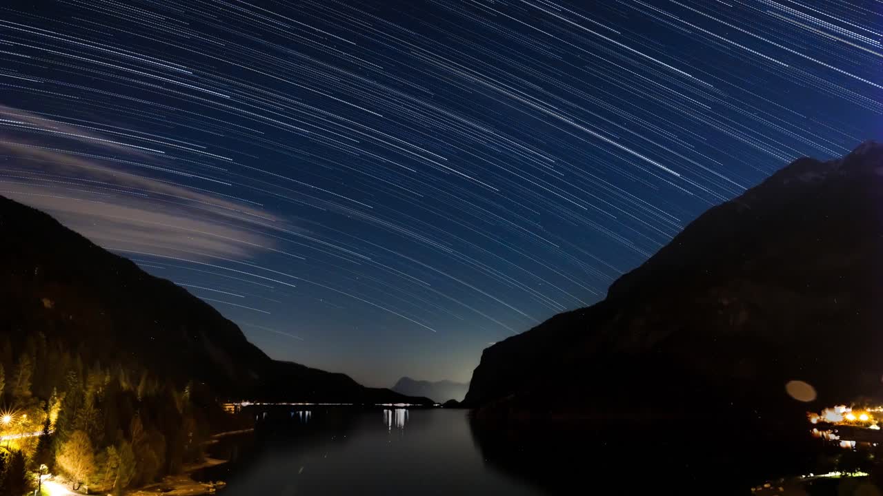 estrelas, trilhas e nuvens passando sobre o lago molveno, em trentino, itália, à noite.