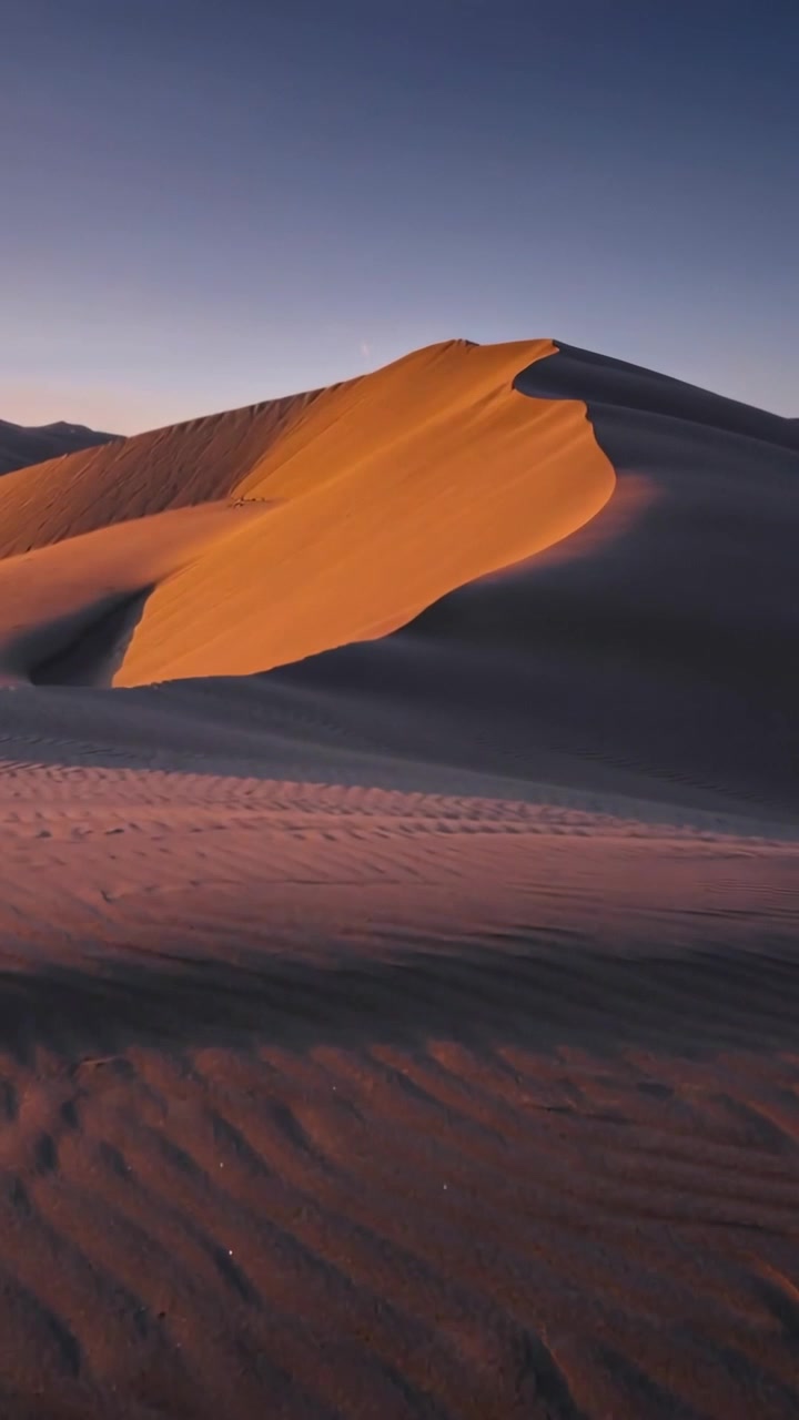 Video verticale: Drone che si alza, rivelando una duna a mezzaluna con sabbia increspata al tramonto, mostrando la cresta