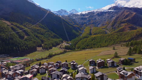 stunning aerial footage of saas-fee in autumn. golden forests surround the alpine village, nestled in the swiss alps. vibrant fall colors and majestic peaks highlight the beauty of the season.
