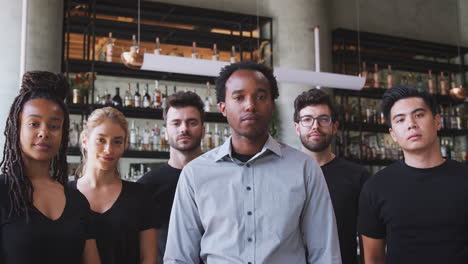 portrait of male owner of restaurant bar with team of waiting staff standing by counter