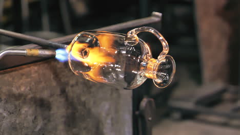 glass artist rotates vase while heating it with blowtorch