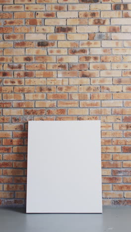 Vertical video of white canvas sign with copy space on floor against brick wall background
