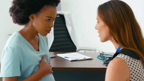 unhappy pregnant woman with depression at appointment with female doctor or gp in office