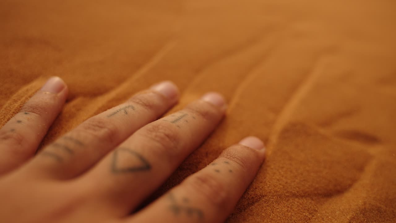 Tattooed hand sinks gently into Sahara sand, capturing its warmth and texture