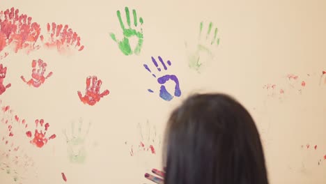 un niño lindo feliz y su joven madre se están divirtiendo dejando sus coloridas huellas de manos en la pared.