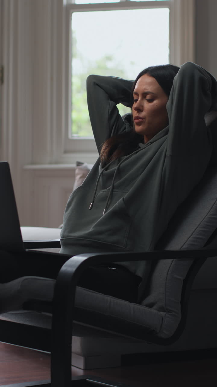 Vertical Video Of Anxious Woman Sitting Indoors On Chair Working From Home Using Laptop Worried About Cost Of Living Crisis