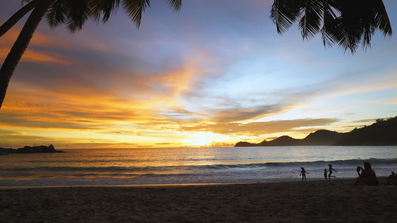 Sunset at takamaka beach under the coconut trees, children playing on the beach on Mahe, Seychelles