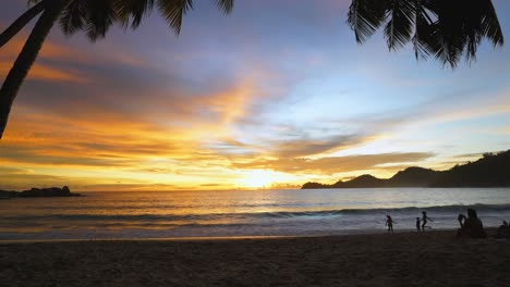 sunset at takamaka beach under the coconut trees, children playing on the beach on mahe, seychelles