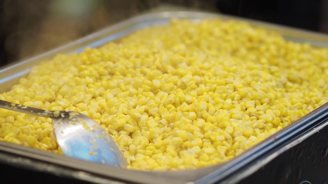 Chicchi di mais dolce fumanti in un vassoio di metallo.