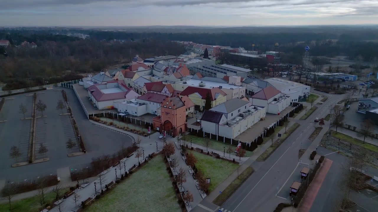 Time-lapse com rampa de velocidade registrando um grande centro comercial outlet com vários edifícios, lojas de varejo e um estacionamento vazio. Vista aérea espetacular de drone em panorama avançando.