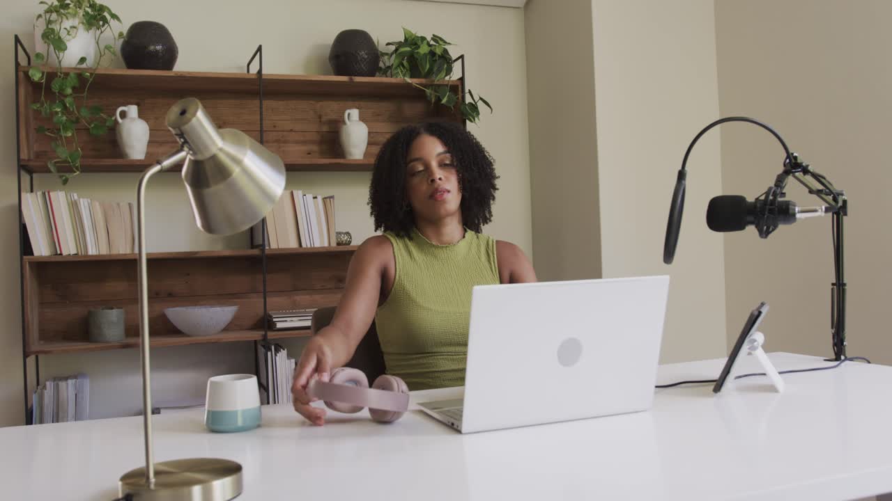 African American woman donning headphones after pausing typing, joining call at home office