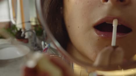 mujer joven poniéndose brillo de labios en los labios con un espejo, reflejo de aplicación de brillo de labios