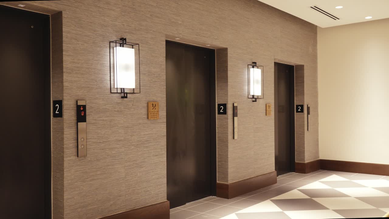 Tracking reveal from a macro wicker texture to a modern hotel elevator bank. Elegant boutique interior featuring textured walls, sconce lighting, and checkered flooring