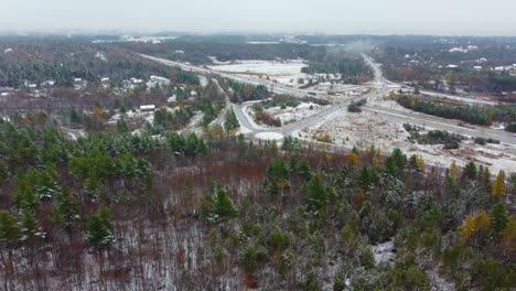 Aerial-view-of-an-autumnal-landscape-with-snow-over-an-intersection-that-crosses-the-forest,-near-Mount-Washington,-New-Hampshire,-USA