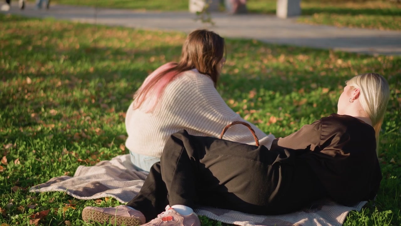To unge kvinder slapper af på et picnictæppe i en park