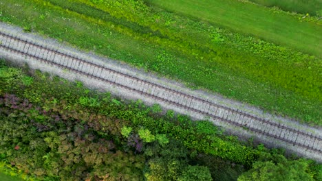 train track through green fields aerial drone top notch circles above rail road