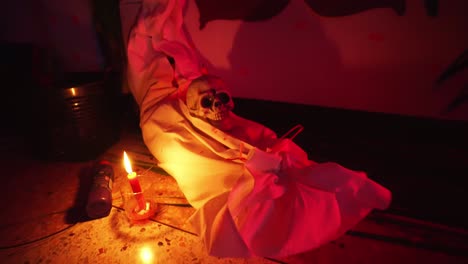 room decorated for halloween party: close-up shot of a skull laying on a dead body with burning candles and red lightning