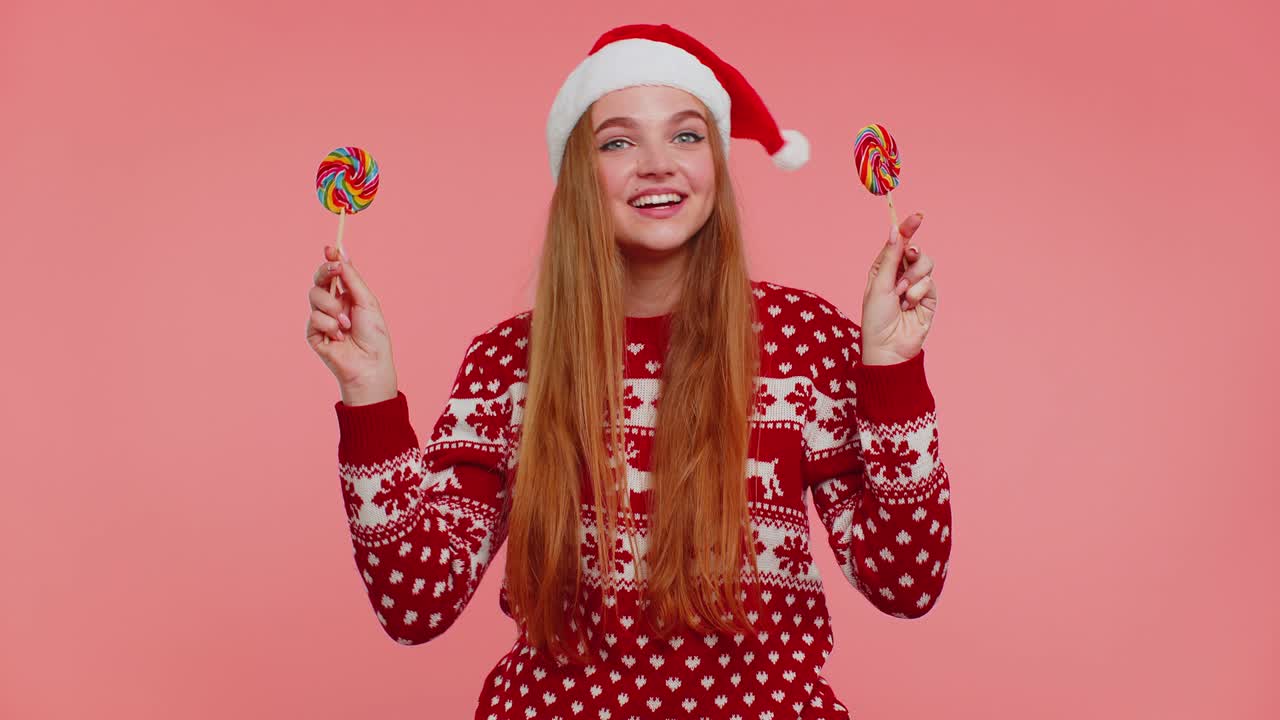 chica divertida en suéter de año nuevo sosteniendo caramelos rayados piruletas escondiéndose detrás de ellos, haciendo tonterías