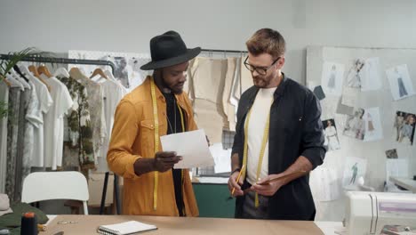 jóvenes y diseñadores de ropa trabajando juntos en una nueva colección en el estudio y sonriendo a la cámara