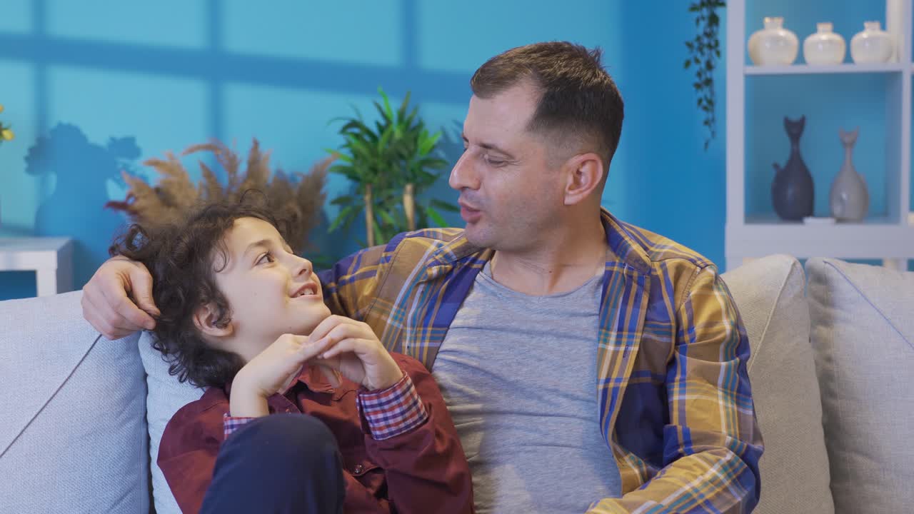 padre adulto amoroso charlando con su niño lindo, divirtiéndose riendo en el sofá.