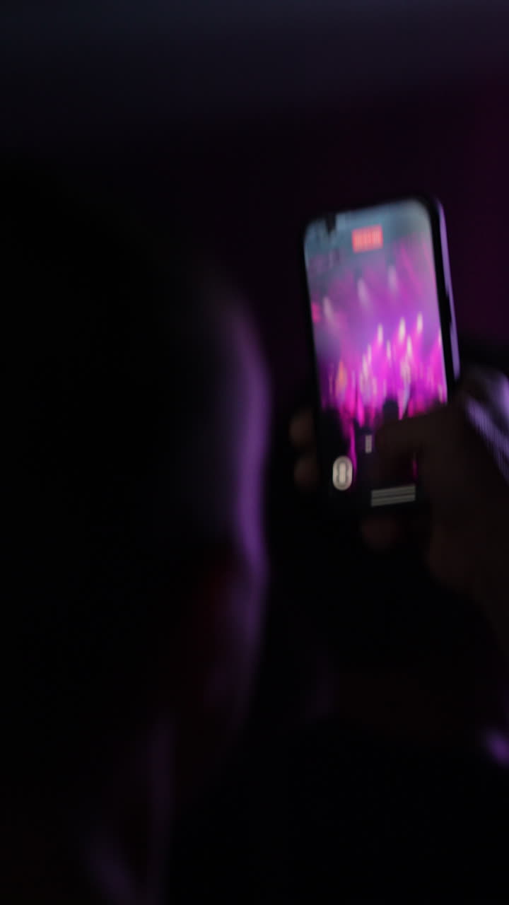 Smartphone optager pulserende koncertoptræden med farverige lys og energisk atmosfære.
