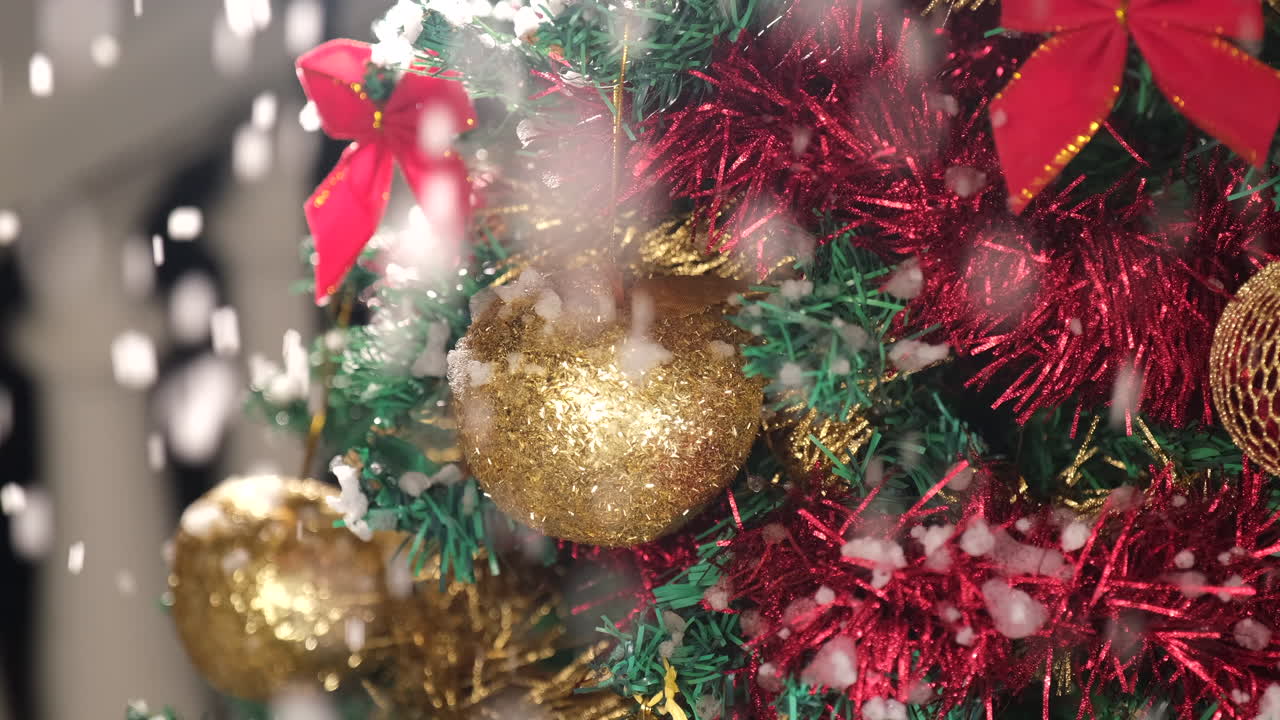 detalle de la bola dorada de navidad en el árbol con nieve cayendo