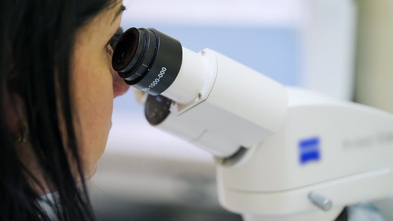 Woman at modern microscope. Close-up microscope in the laboratory. Medical assistant looking through the contemporary device. New technologies in medicine.