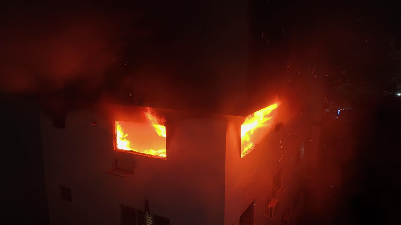 Static drone shot of flames coming out from a apartment window, during night