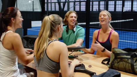 group of friends relaxing after padel tennis match, chatting and smiling together, on indoor court